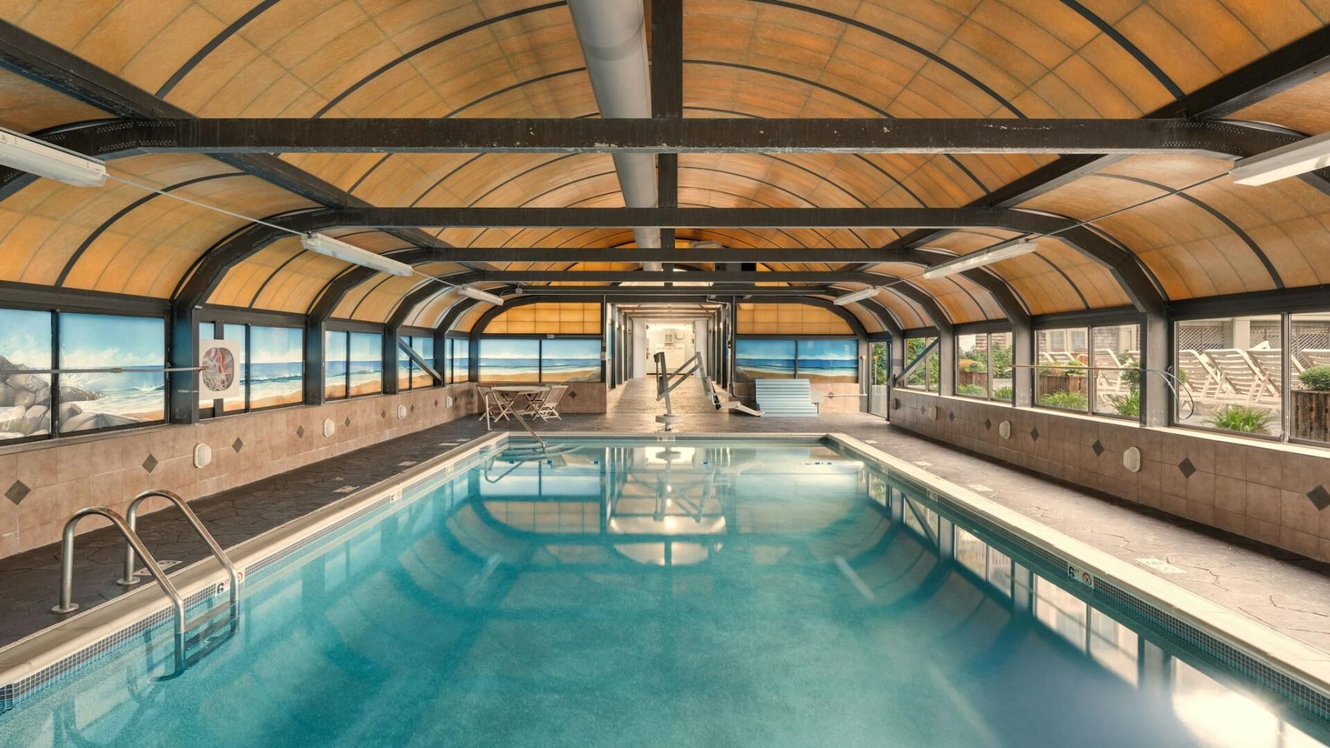 An indoor swimming pool with a view of the beach through large windows.