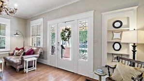 Un salon avec un canapé en cuir, une table d’appoint blanche, un banc en bois et un lustre.