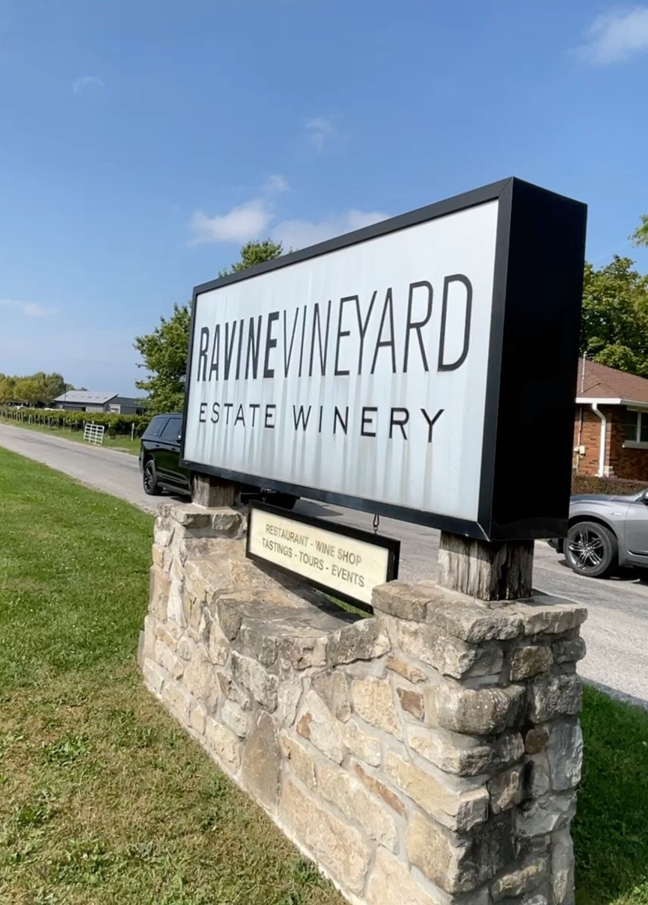 A sign for Ravine Vineyard Estate Winery with a stone base, listing amenities like a restaurant, wine shop, tastings, tours, and events.