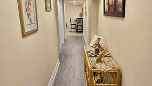 A hallway with wooden flooring, framed artwork on the walls, and a small table with a decorative item. - Charming B&B with WiFi/Kitchenette and AC in Marvelous Niagara-on-the-Lake (Niagara-on-the-Lake)