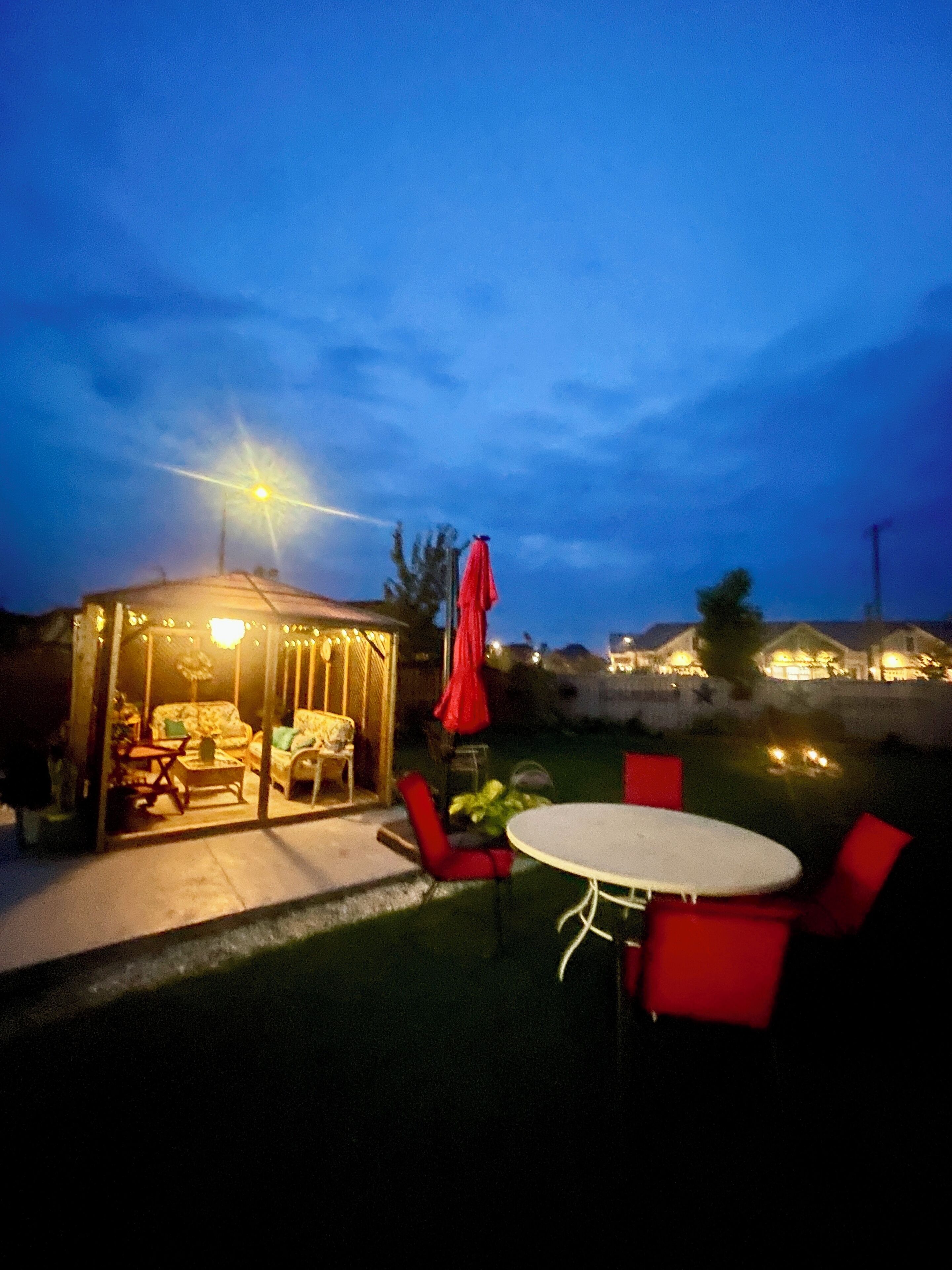 An outdoor patio area with a covered seating area, a round table, and red chairs.