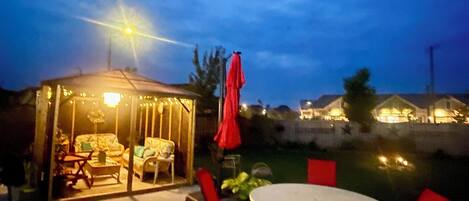 An outdoor patio area with a covered seating area, a round table, and red chairs.