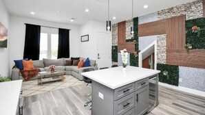 Una sala de estar moderna con un sofá gris, una mesa de centro y una zona de cocina con armarios grises y una encimera blanca.