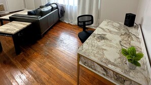 Una sala de estar con un sofá, una mesa de comedor con cubierta de mármol, una silla negra y una planta.