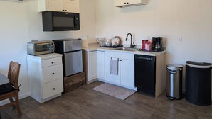 Une cuisine compacte dotée de meubles blancs, d’un four à micro-ondes, d’un grille-pain, d’un réfrigérateur, d’un évier et d’un lave-vaisselle.