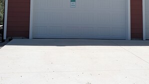 Une porte de garage blanche avec une pancarte indiquant « Parking réservé aux invités », un bâtiment brun et un ciel dégagé.