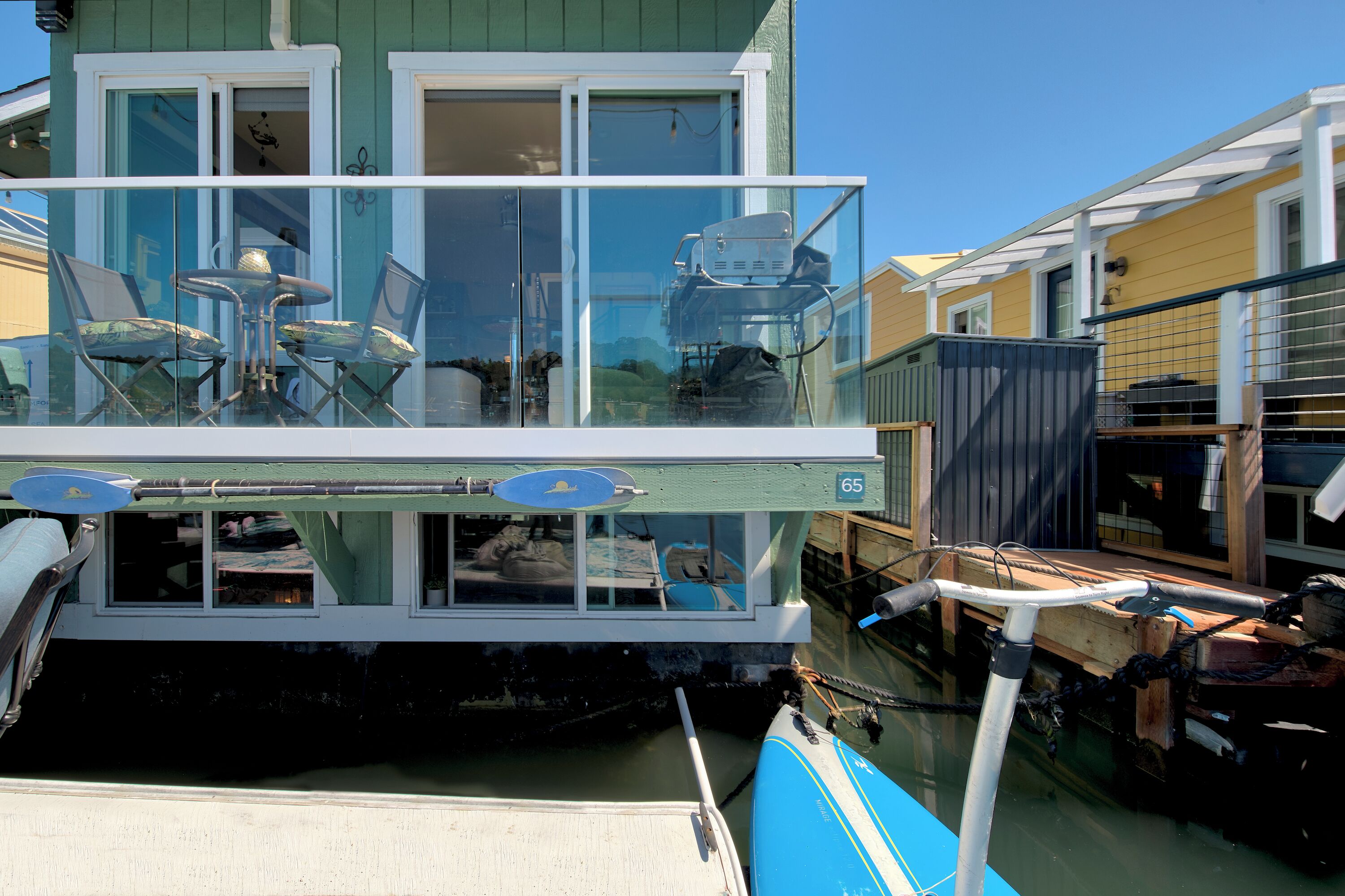 Ein schwimmendes Haus mit Glasbalkon, Essbereich und der Nummer 65 an der Seite.