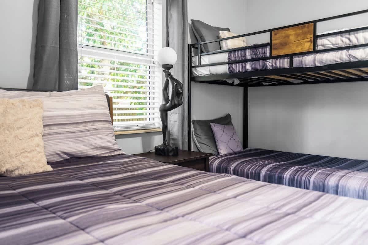 A room with a bunk bed, a single bed, and a bedside table with a lamp.