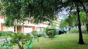 A courtyard with a building in the background, surrounded by greenery and a parked car. - Limoges,, T2 ++parkings au Jardin ,,acces Facile ! (Limoges)