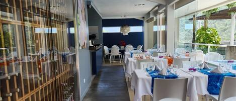 Un long couloir avec des tables dressées pour le repas, un meuble à vin sur la gauche et une vue sur l’extérieur grâce à de grandes fenêtres.