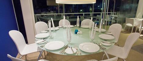 A round glass table with white chairs, set for a meal.