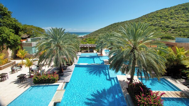 A resort pool area with multiple swimming pools, palm trees, and a view of the ocean.