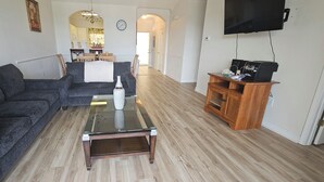 Sala de estar com sofá seccional cinza escuro, mesa de centro de vidro e armário de madeira com dispositivos eletrônicos.