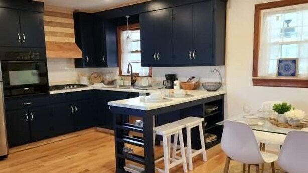 Una cocina moderna con armarios oscuros, piso de madera y una isla central con taburetes.