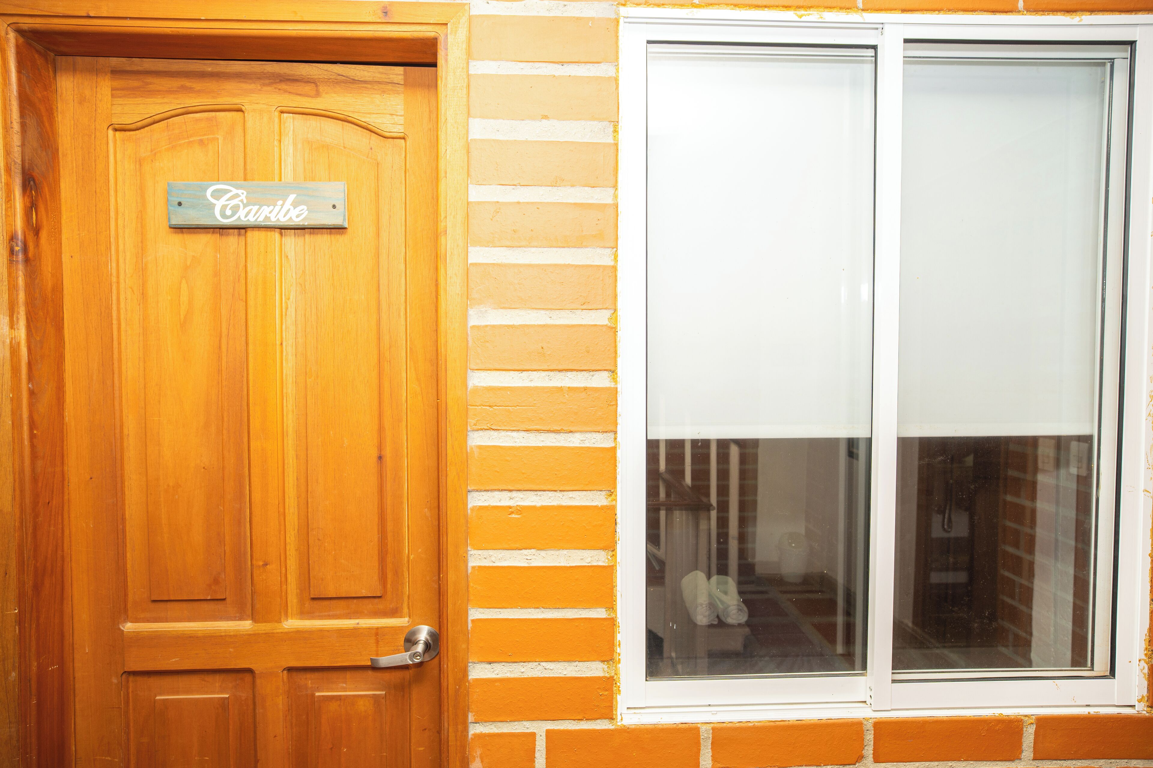 Eine Holztür mit einem 'Caribe'-Schild, ein Fenster mit Blick auf eine Treppe und eine Ziegelwand.