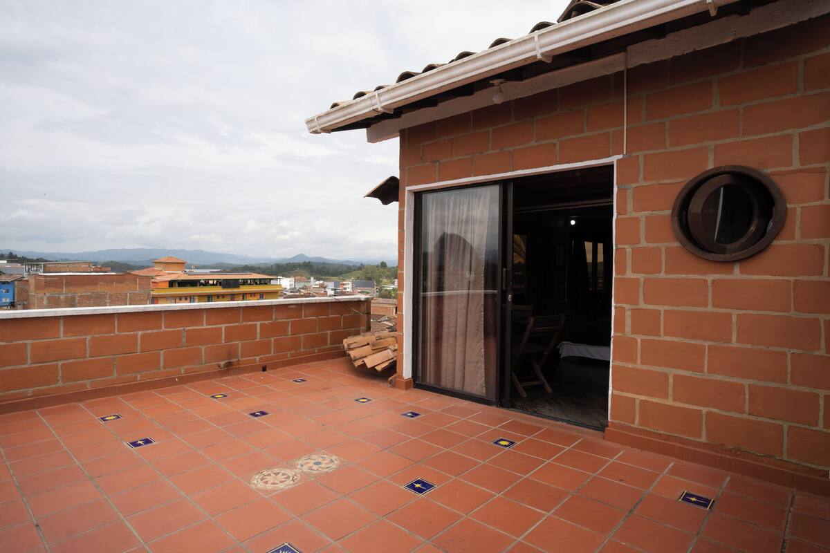 Terraço no telhado com parede de tijolos, porta de vidro deslizante e vista para montanhas distantes.