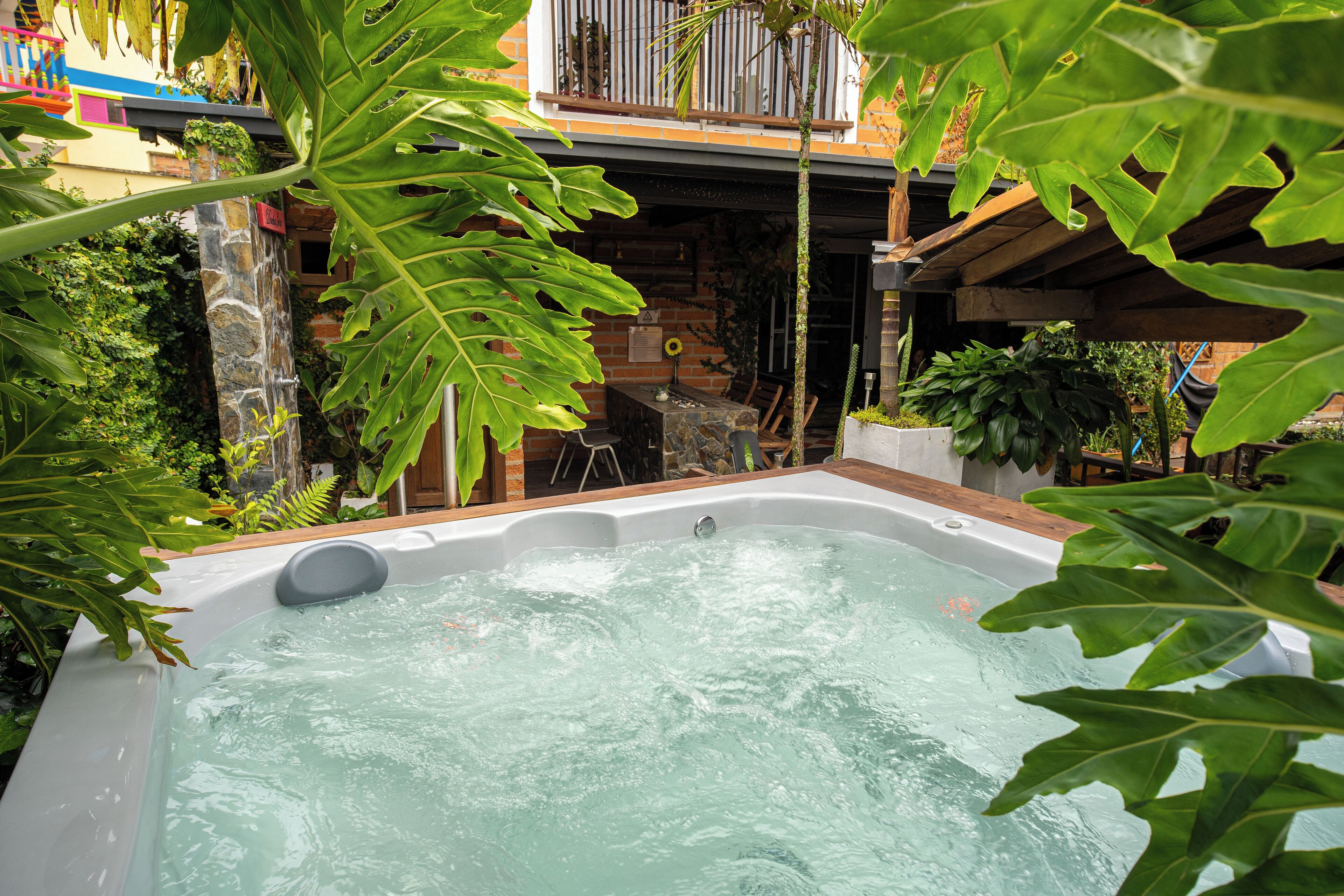 A hot tub surrounded by lush greenery, stone walls, and a wooden deck.
