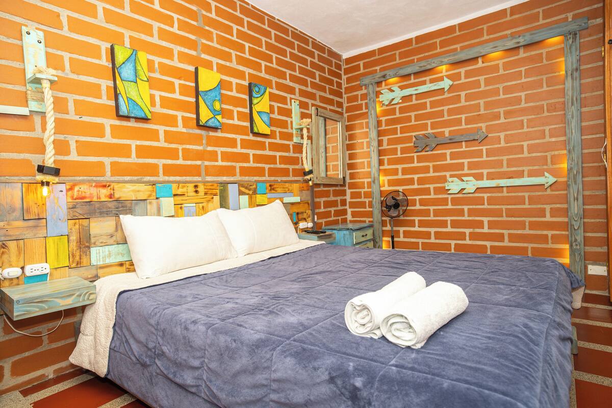Um quarto com parede de tijolos, cama com colcha azul e cabeceira de madeira.