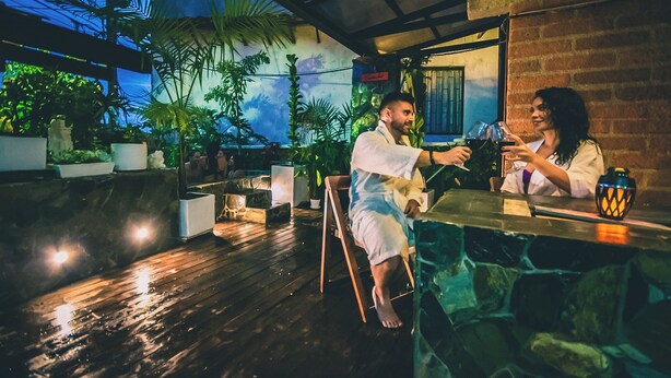 Una pareja sentada en un bar con vistas a plantas tropicales y un muro de ladrillo.