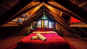 Un dormitorio en el ático con una cama roja, vigas de madera y un tragaluz.