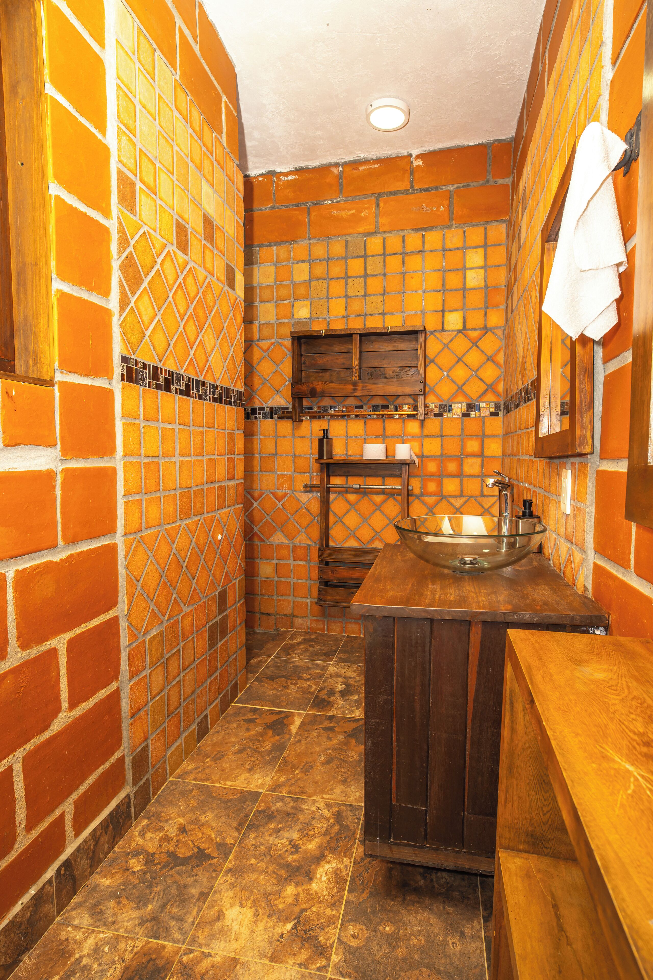A bathroom with a tiled wall, a wooden vanity, a sink, and a mirror.