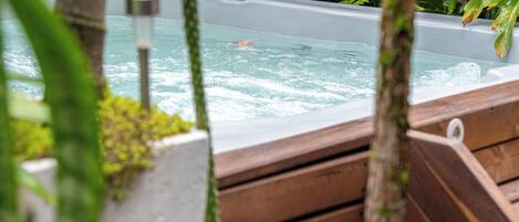 A hot tub surrounded by lush greenery and wooden benches.