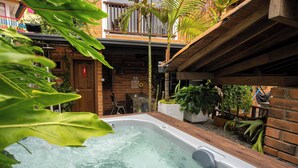 Un jacuzzi en un jardín con paredes de ladrillo, terraza de madera y varias plantas.