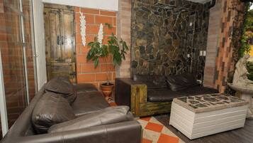 A living room with a brown leather sofa, a white ottoman, a potted plant, and a stone wall.