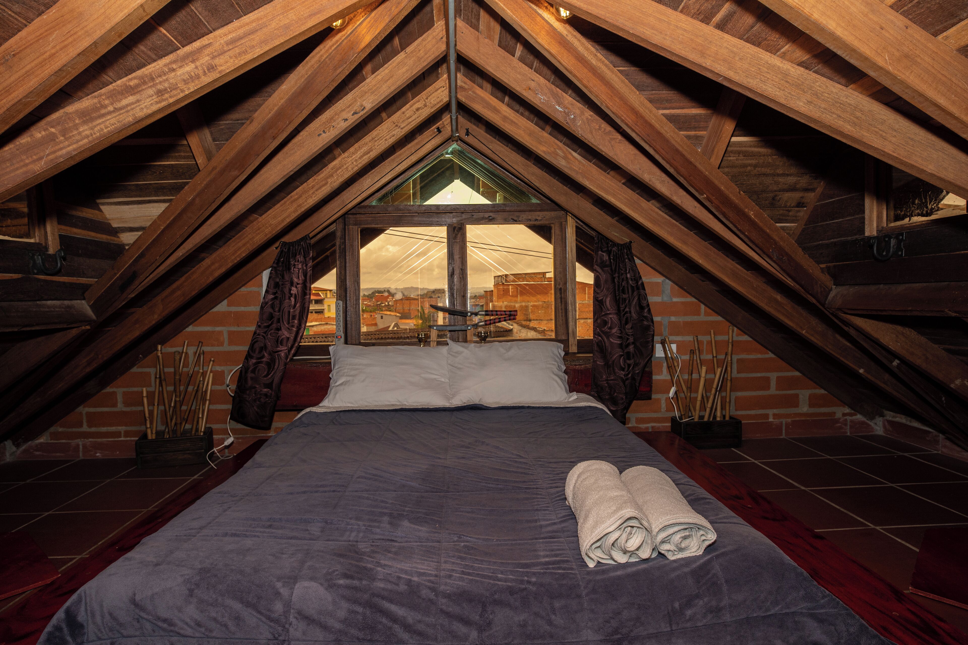 A bedroom with a sloped ceiling, a bed, pillows, a window, and a view of the outside.