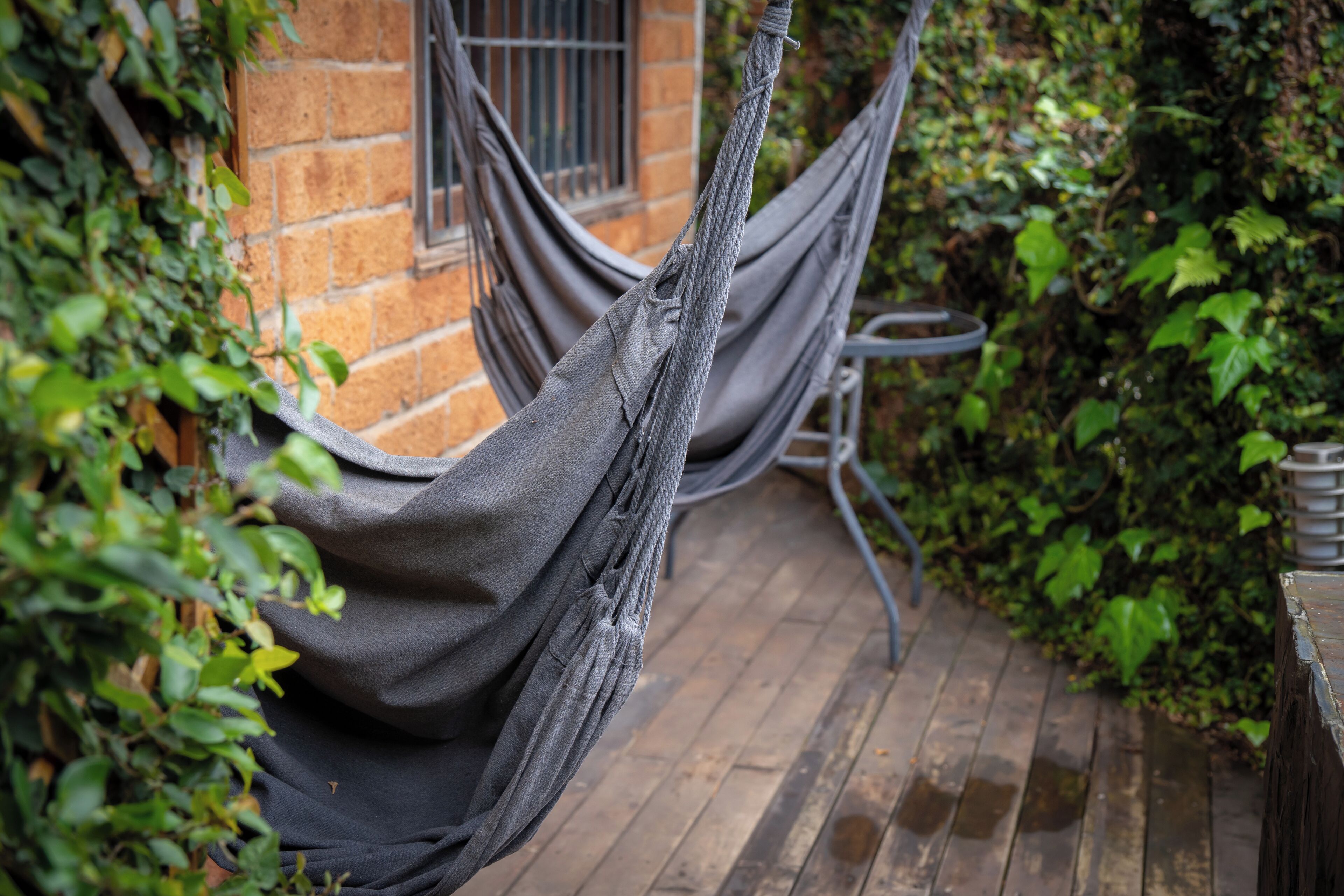 Una hamaca atada entre dos muros de ladrillo en un jardín con terraza de madera y follaje.
