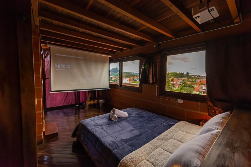Een slaapkamer met een bed, een projectiescherm en uitzicht op een stad door een raam.