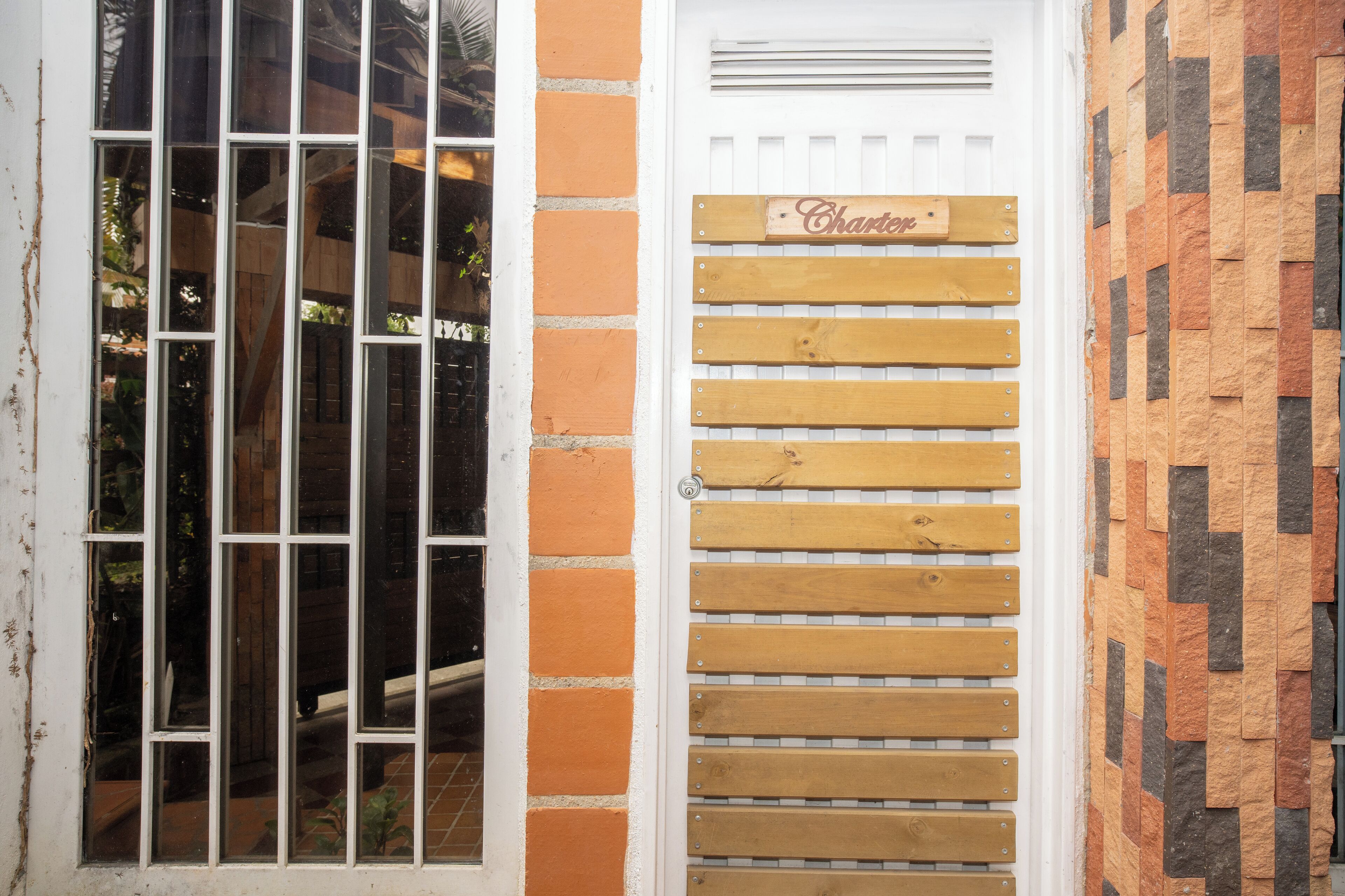 Una puerta con un letrero de madera, una ventana con barrotes y un muro de ladrillo.