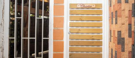 Una puerta con un letrero de madera, una ventana con barrotes y un muro de ladrillo.