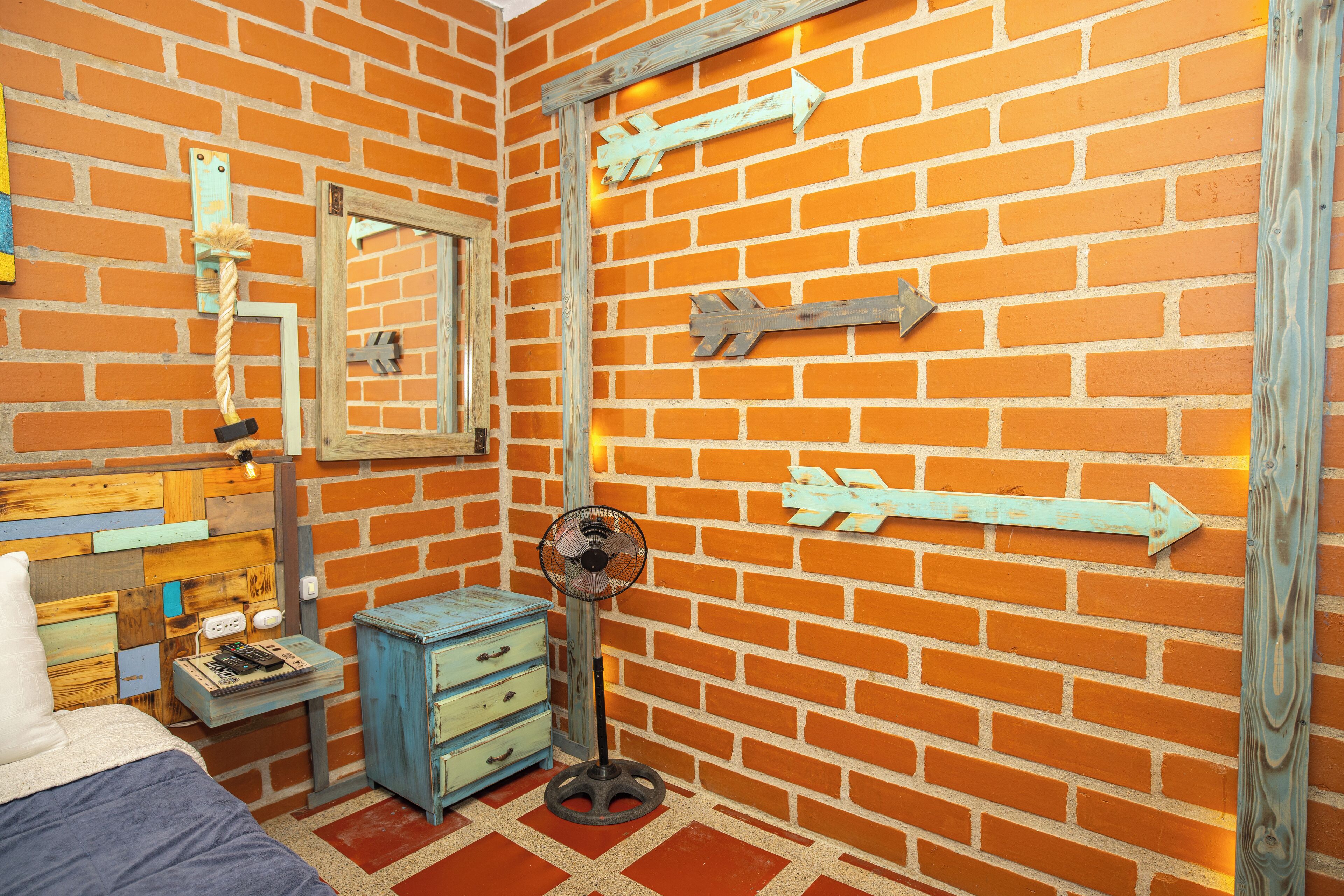 A room with a brick wall, a bed, a dresser, and a fan.
