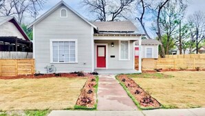 A single-story house with a red door, a front porch, and a small front yard with a pathway.