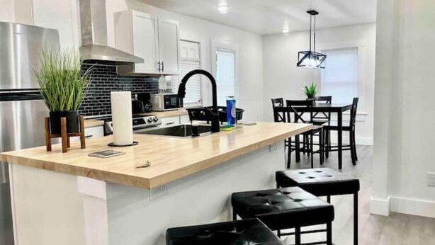 A modern kitchen with a wooden island, stainless steel appliances, and black bar stools.