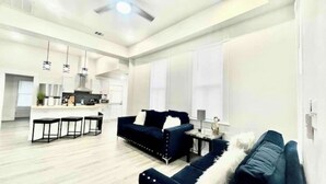 A modern living room with a sofa, a coffee table, and a dining area with a kitchen in the background.