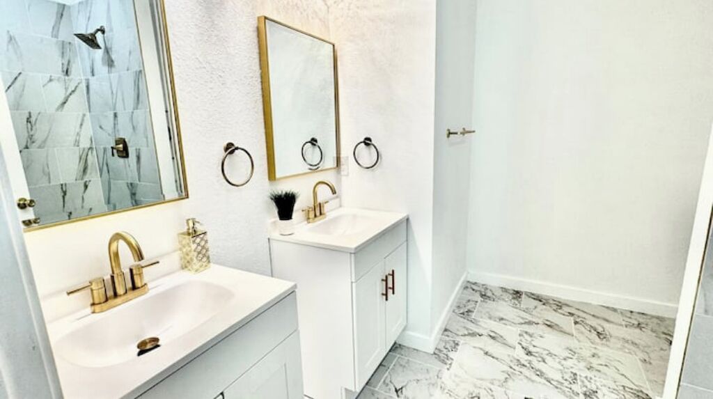 A bathroom with two sinks, a mirror, and a shower.