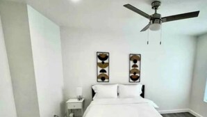 A bedroom with a bed, a nightstand, a ceiling fan, and two wall-mounted decorative items. - 6 min downtown New home (San Antonio)