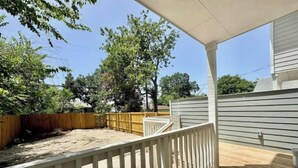 A wooden deck with a white railing, a sandy backyard, and a gray building in the background. - 6 min downtown New home (San Antonio)