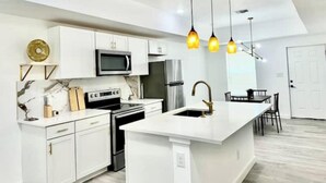 A modern kitchen with white cabinetry, a central island, stainless steel appliances, and pendant lighting. - Brand new home 6 min downtown (San Antonio)