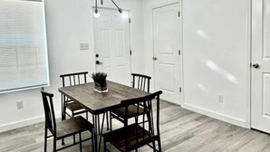 A dining area with a wooden table and chairs, a modern chandelier, and white walls. - Brand new home 6 min downtown (San Antonio)