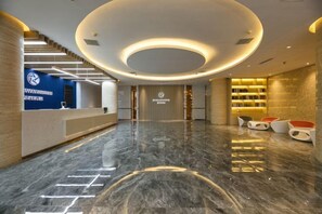 A hotel lobby with a reception desk, a staircase, and a seating area with bookshelves. - Starway Hotel (Hangzhou Binjiang Jiangnan Avenue) (Hangzhou)