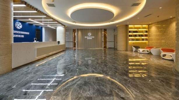 Una hall d'albergo moderna con una reception, una scala, un'area salotto con poltrone arancioni e una libreria.