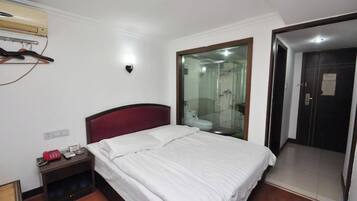 A hotel room with a bed, a nightstand, a mirror, and a door leading to a bathroom.