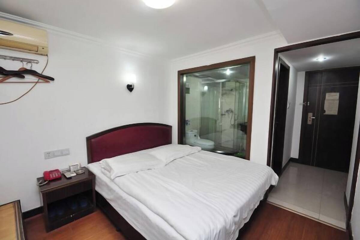 A hotel room with a bed, a nightstand, a mirror, a door, and a shower area.