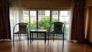 A room with two wicker chairs and a small table, large windows with curtains, and a view of greenery outside. - Tianjiu Hotel (Cixi)