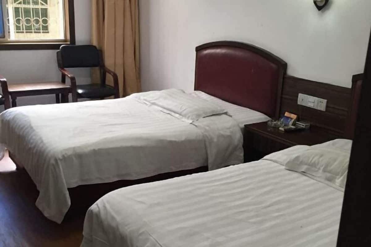 A room with two single beds, a wooden nightstand, a chair, and a window with bars.
