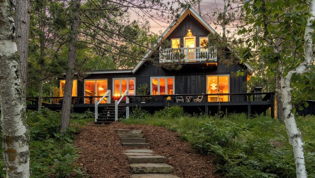 A cabin with a wooden exterior, a balcony with seating, and a stone staircase leading to the entrance.
