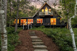 A cabin with a wooden exterior, a balcony with seating, and a stone staircase leading to the entrance.
